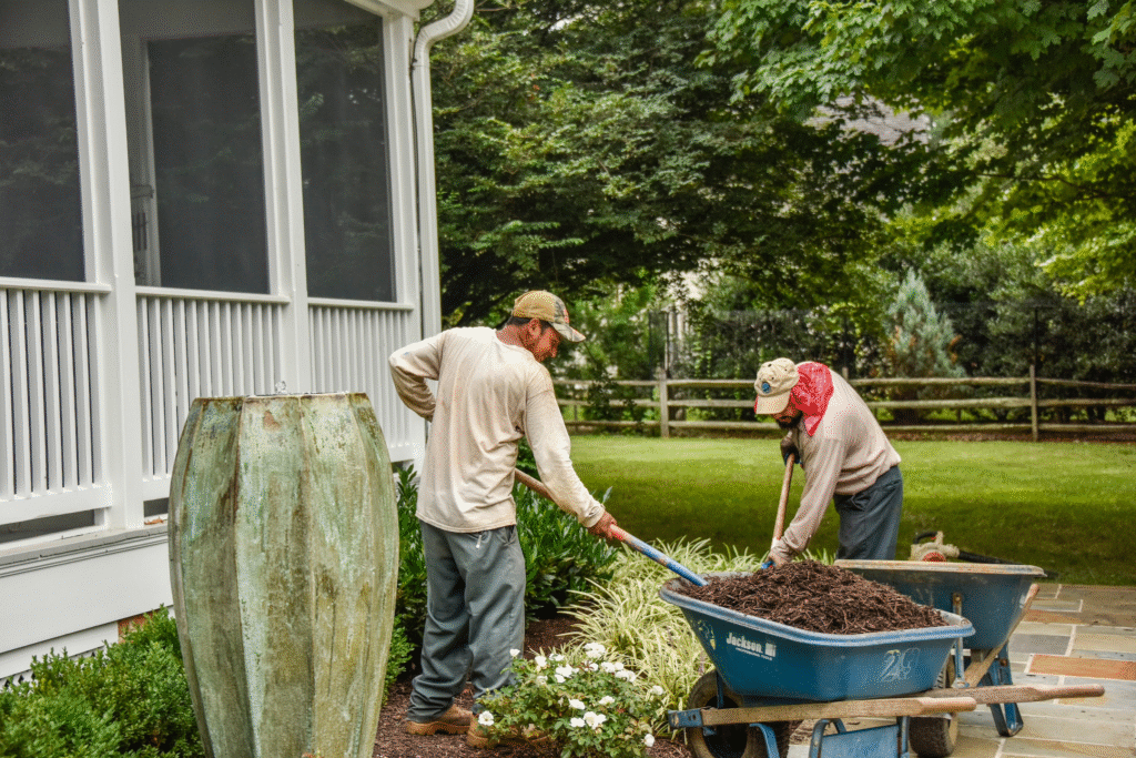 Two men spreading mulch in a flower bed.