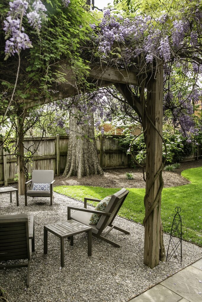 Decorative Gravel Patio Seating with Custom Pergola with Wisteria Lush Turf Area Lawn Landscape Plantings