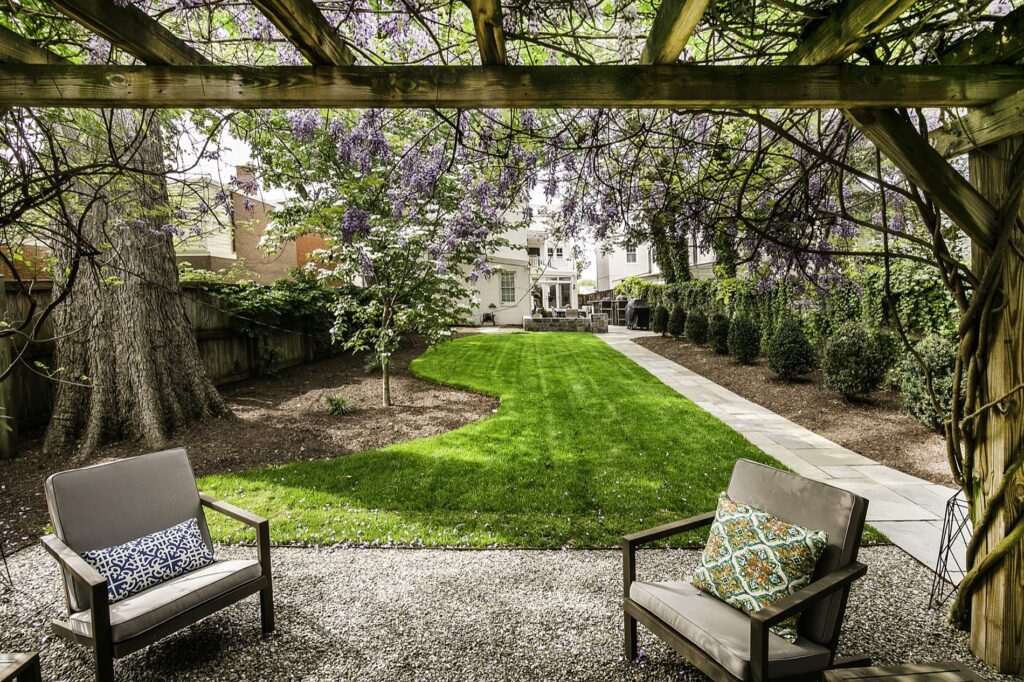 Decorative Gravel Patio Seating with Custom Pergola with Wisteria Lush Turf Area Lawn Landscape Plantings Flagstone Walkway