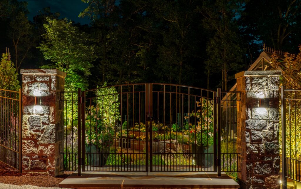 Stone Piers and Iron Entry Gate with LV Lighting Landscape Plantings Low Voltage Landscape Lighting Wrought Iron Fencing