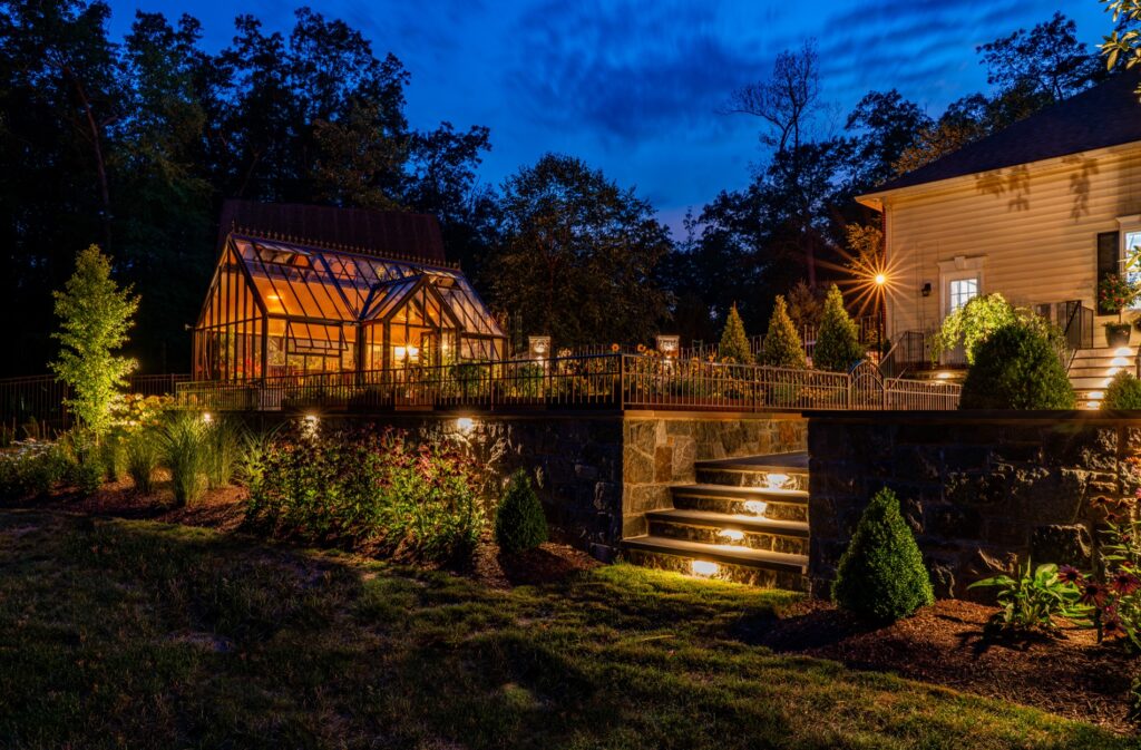 Hartley Botanic Glass Greenhouse at night with lighting Stone Retaining Walls Landscape Plantings Low Voltage Landscape Lighting