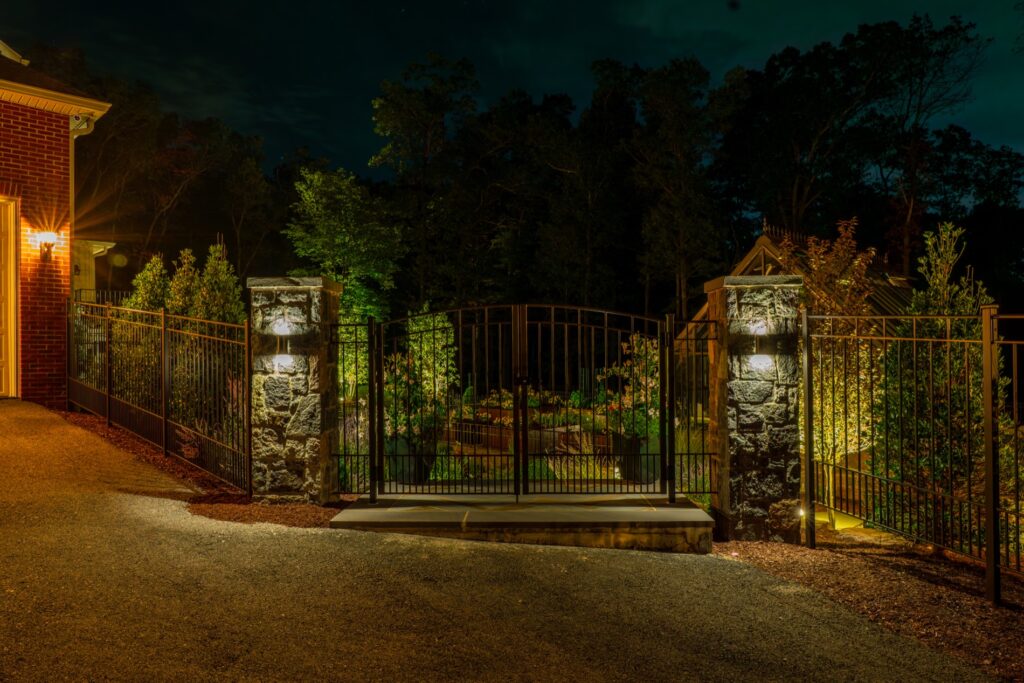 Stone Piers and Iron Entry Gate with LV Lighting Landscape Plantings Wrought Iron Fencing