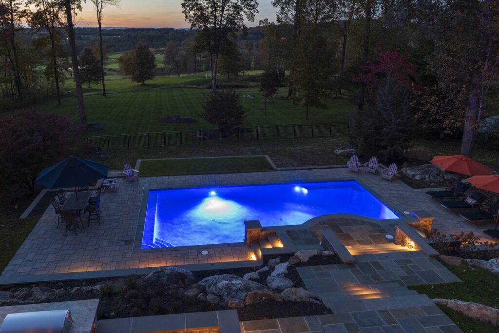 Swimming pool in backyard with paver pool deck flagstone walkway and stone steps low voltage lighting